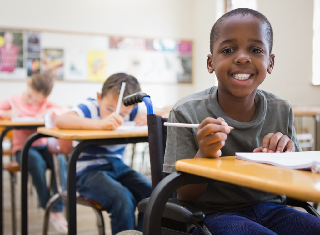 young black student in wheelchair smiling at his desk
