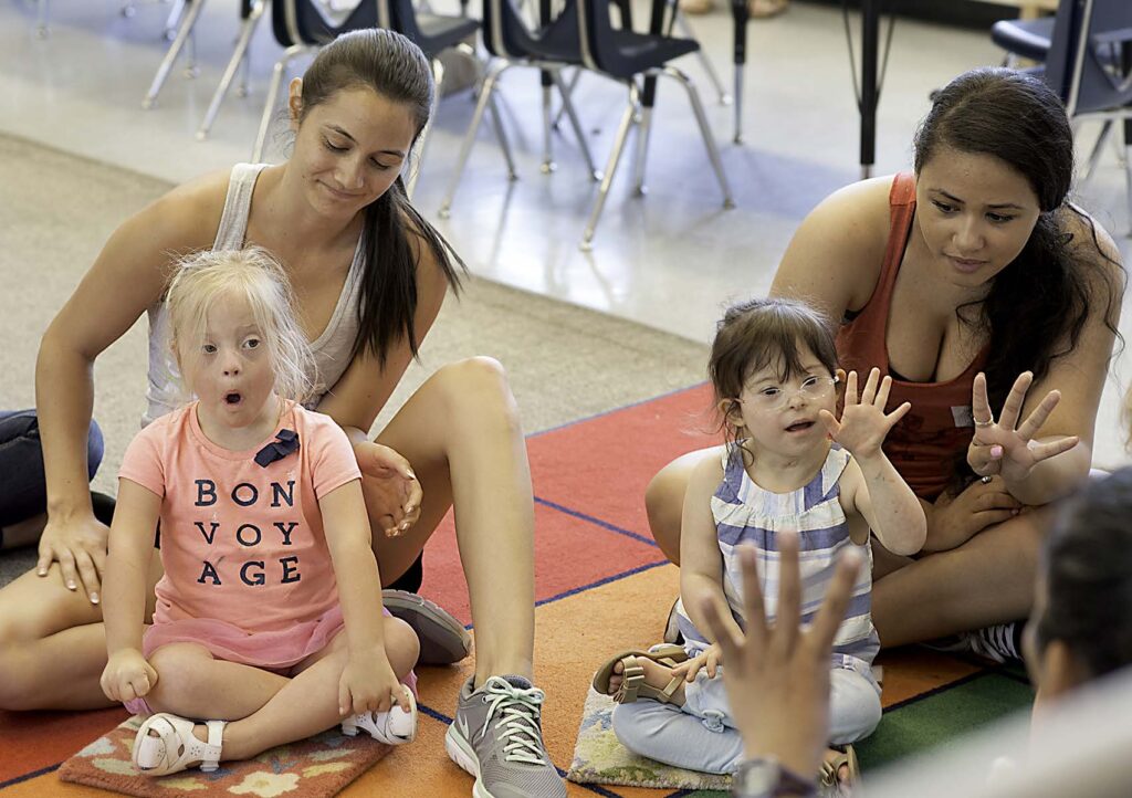 two girls with Down syndrome sit by volunteers