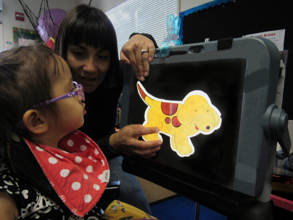 a young girl with a disability interacts with an education device showing an image of a cartoon dog